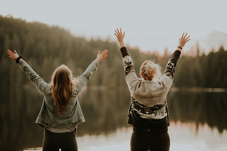 Two women with their hands up in front of a lake